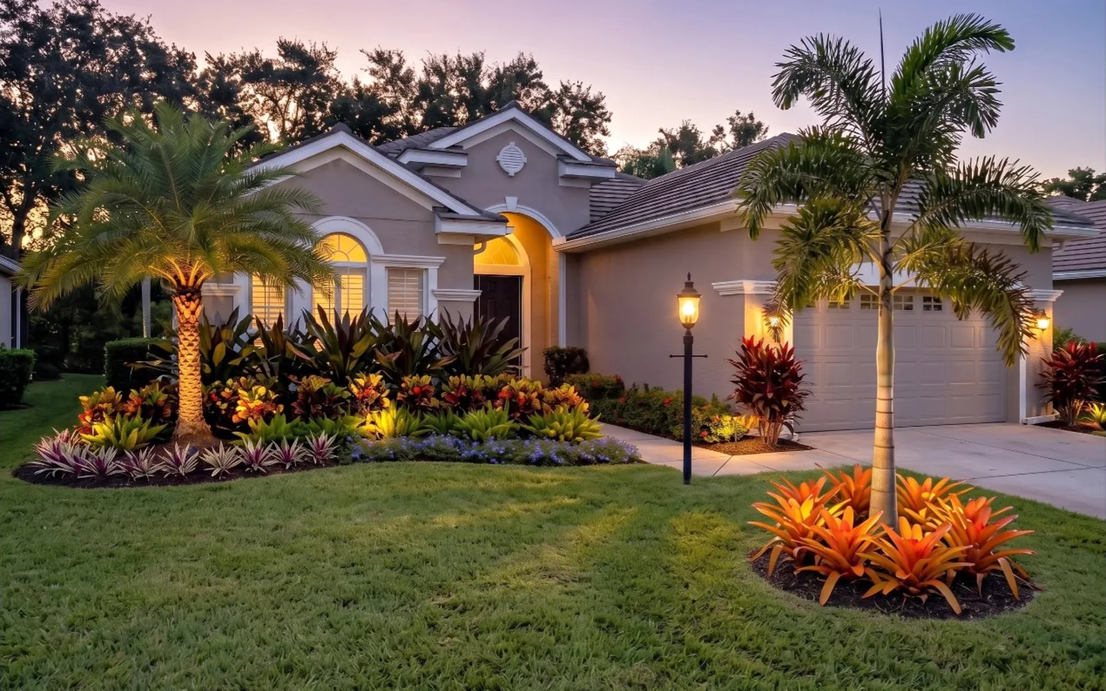 Front landscape at dusk with lit palms, bromeliads and tropical beds at a Florida home